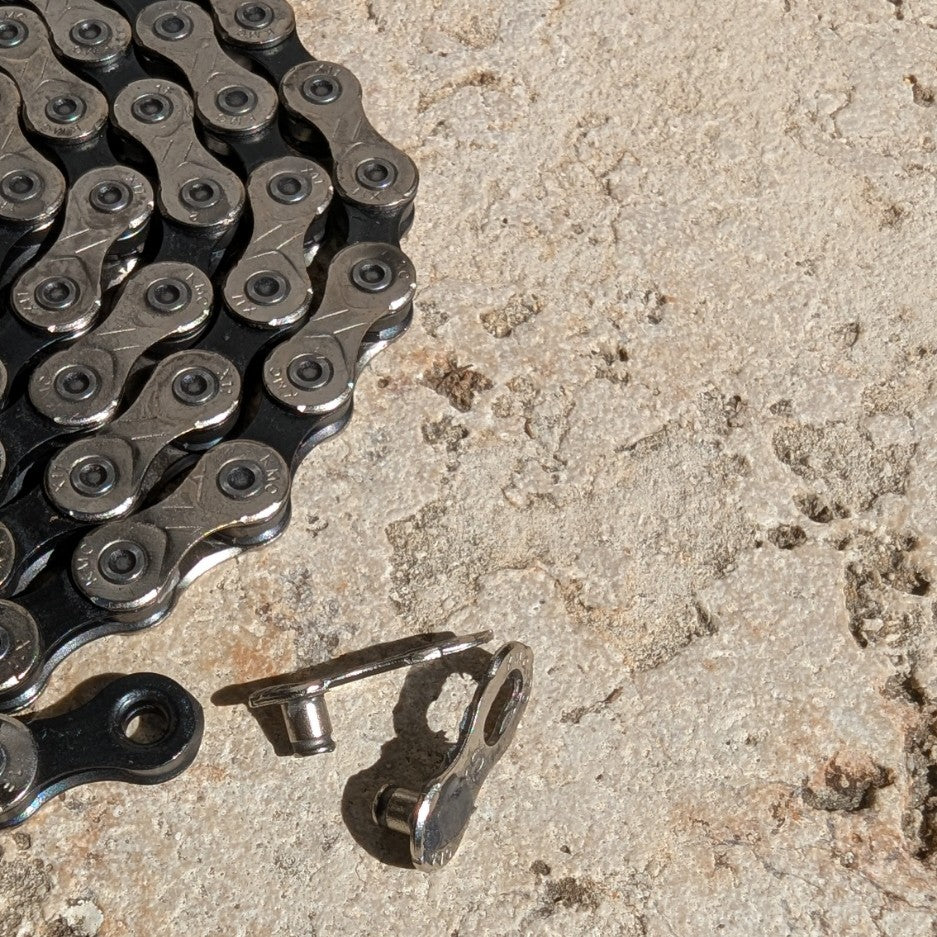 KMC MissingLink 11R CL555R Kettenschloss neben KMC X11 Fahrradkette, Detailaufnahme auf Steinuntergrund