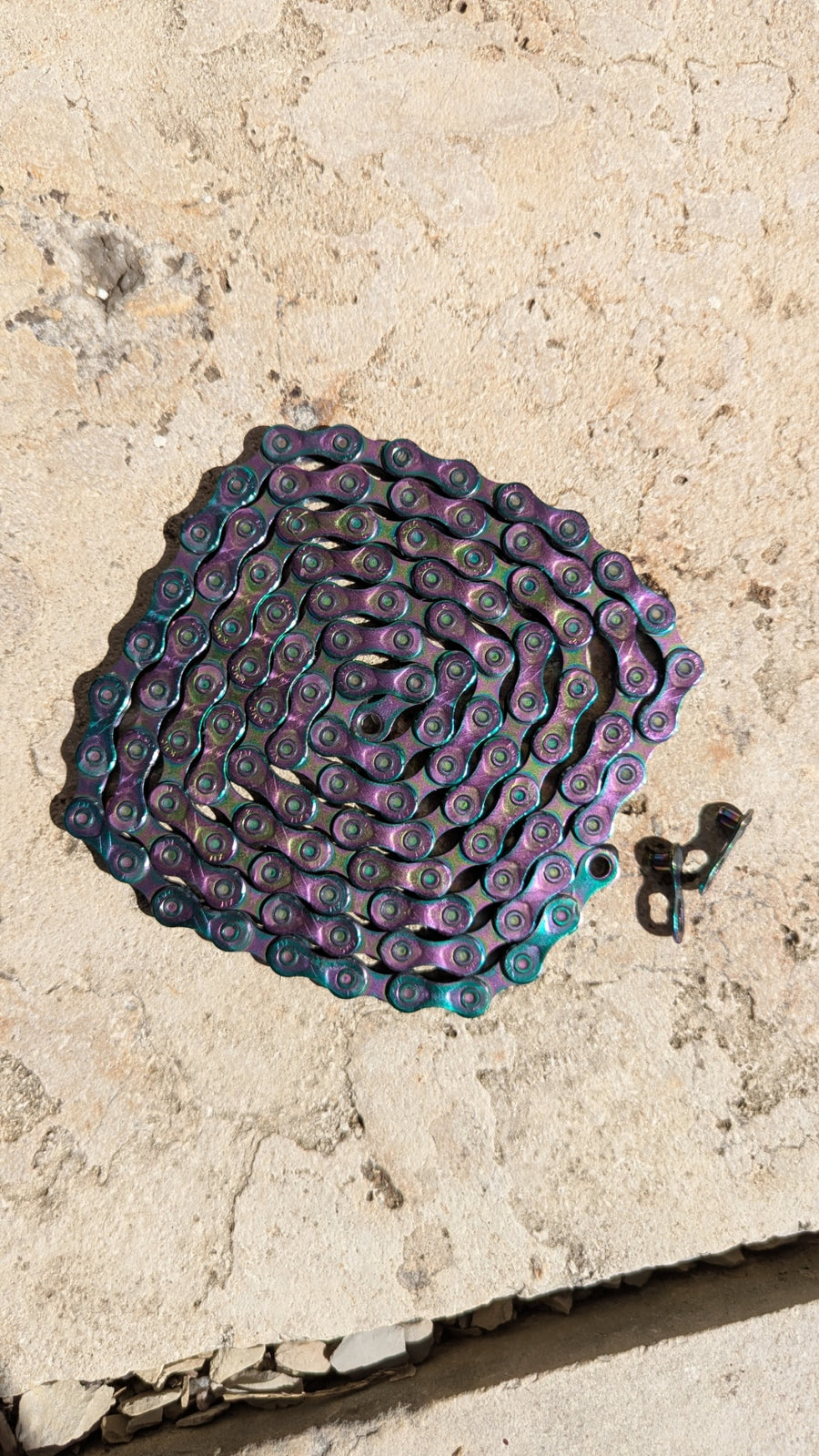 KMC X11 Aurora 11-fach Fahrradkette in Aurora-Farbfinish, professionell mit Molten Speed Wax behandelt, ausgelegt mit Kettenschloss auf Steinuntergrund