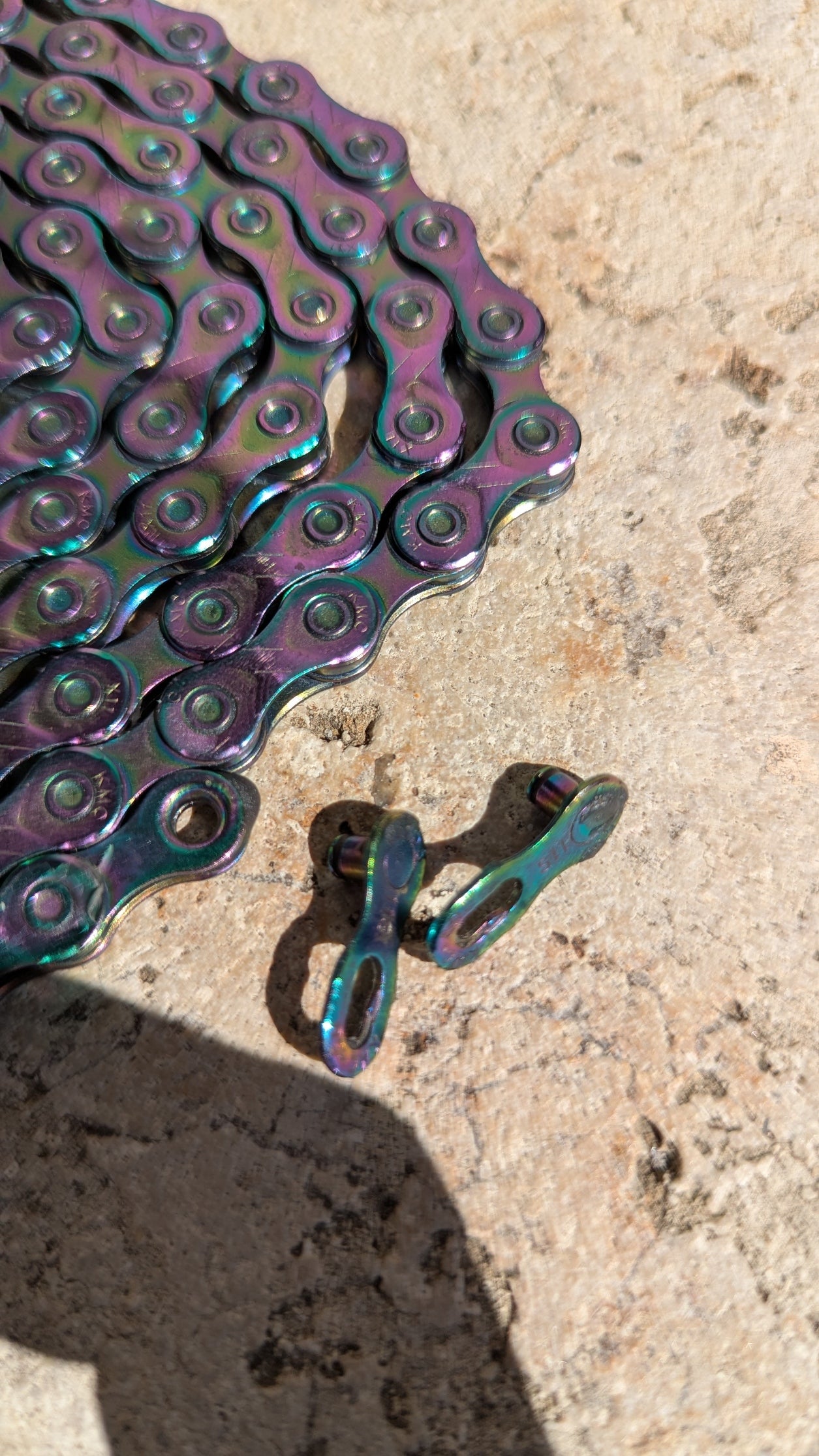 Detailaufnahme der KMC X11 Aurora 11-fach Fahrradkette mit Aurora-Farbfinish und passendem MissingLink Kettenschloss auf Steinuntergrund