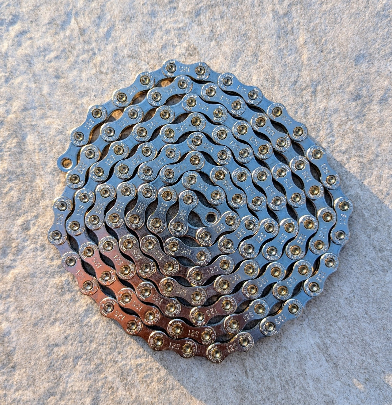 Mit Molten Speed Wax behandelte Cycling Components CN/Twelve SLV 126 TW 12-fach Fahrradkette eingerollt auf hellem Untergrund