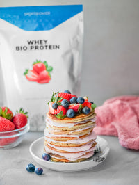 Protein-Pancakes mit Erdbeercreme und frischen Beeren, angerichtet auf einem Teller vor einer Packung Sportbionier Whey Bio Protein Erdbeere