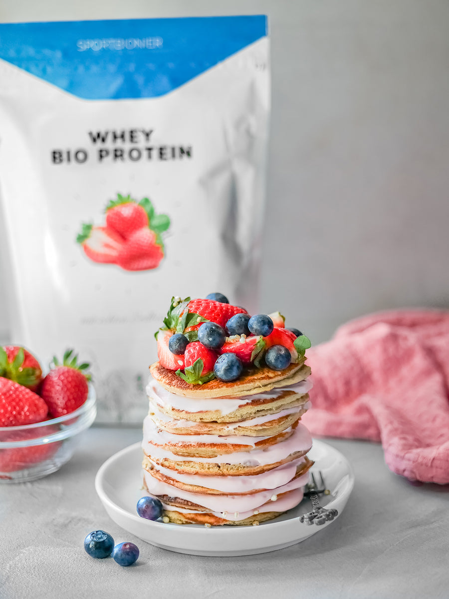 Protein-Pancakes mit Erdbeercreme und frischen Beeren, angerichtet auf einem Teller vor einer Packung Sportbionier Whey Bio Protein Erdbeere